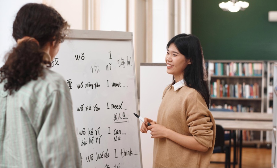 Seorang guru muda mengajar bahasa Mandarin kepada siswi di ruang kelas modern, mencerminkan tren kemudahan belajar bahasa asing secara langsung dan digital di tahun 2025.